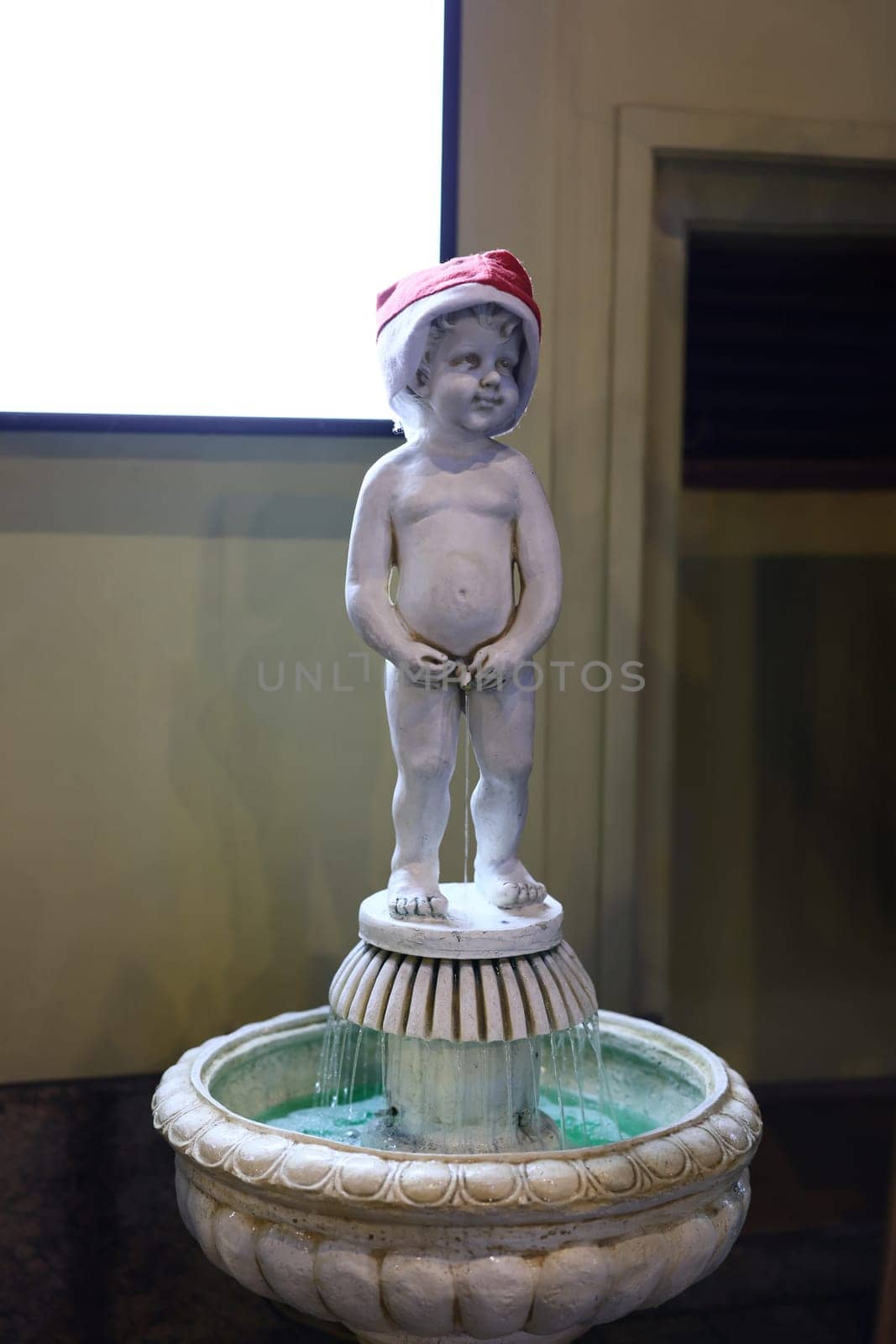 A charming and cute boy statue elegantly standing in a beautiful fountain, adorned with a cheerful holiday hat