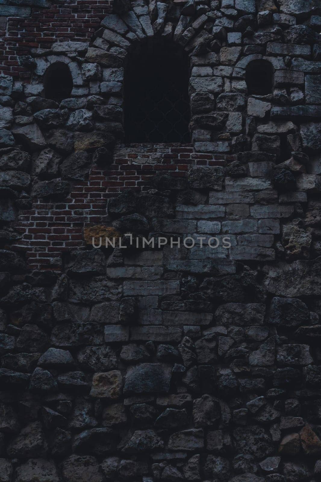 Close-up of an ancient stone and brick wall featuring a dark arched window, weathered texture, and intricate masonry.