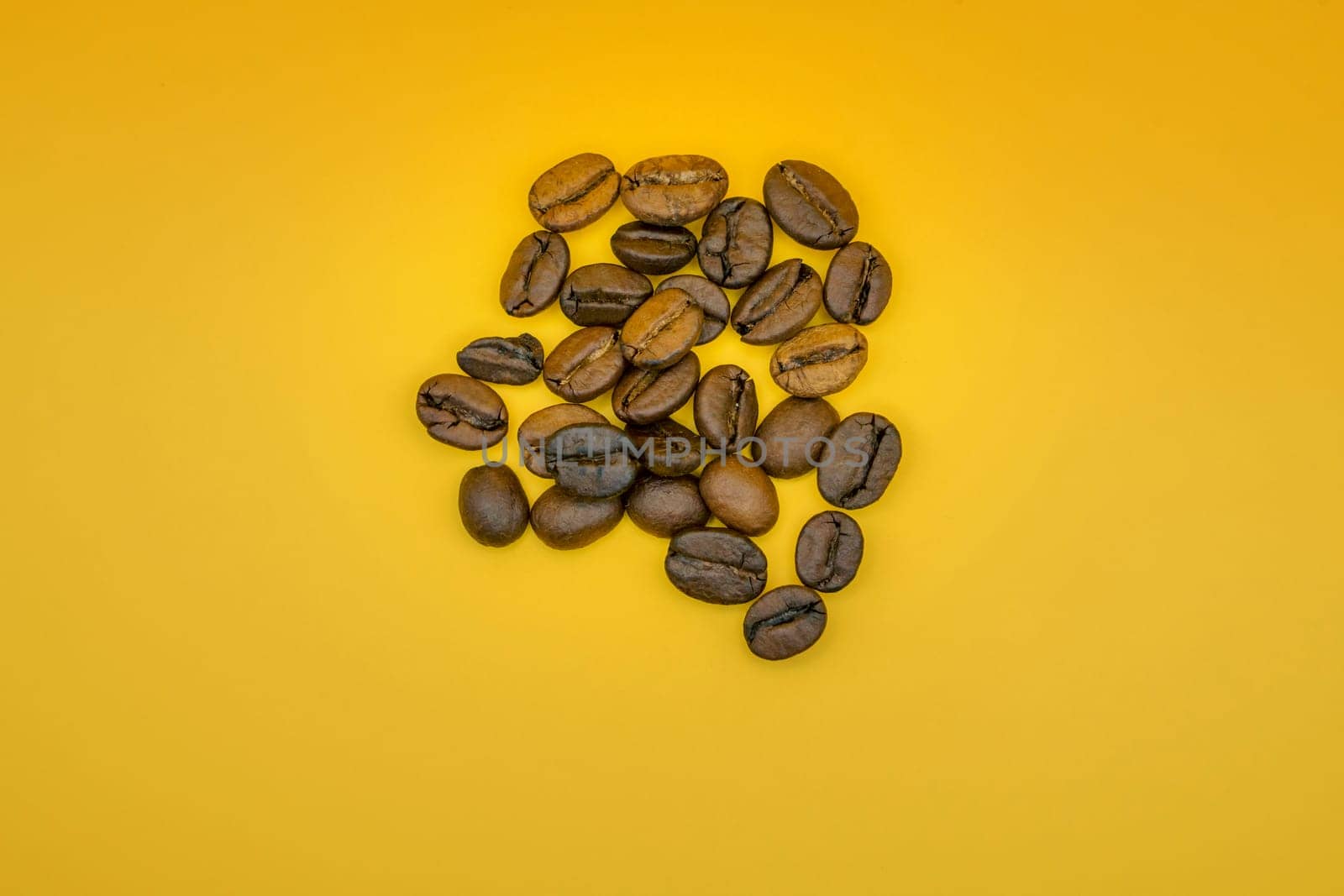 Minimalist arrangement of roasted coffee beans scattered on a vibrant yellow background, highlighting their rich texture and brown tones.