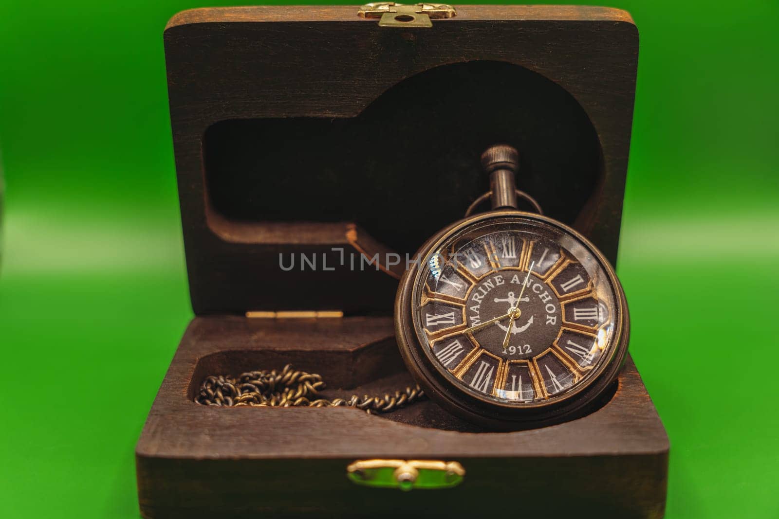 Vintage pocket watch marked "Marine Anchor 1912" with Roman numerals, displayed inside an open wooden case against a green background.