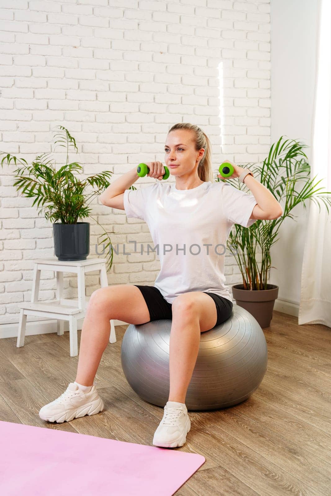 Woman exercising with dumbbells on a stability ball in a bright indoor space