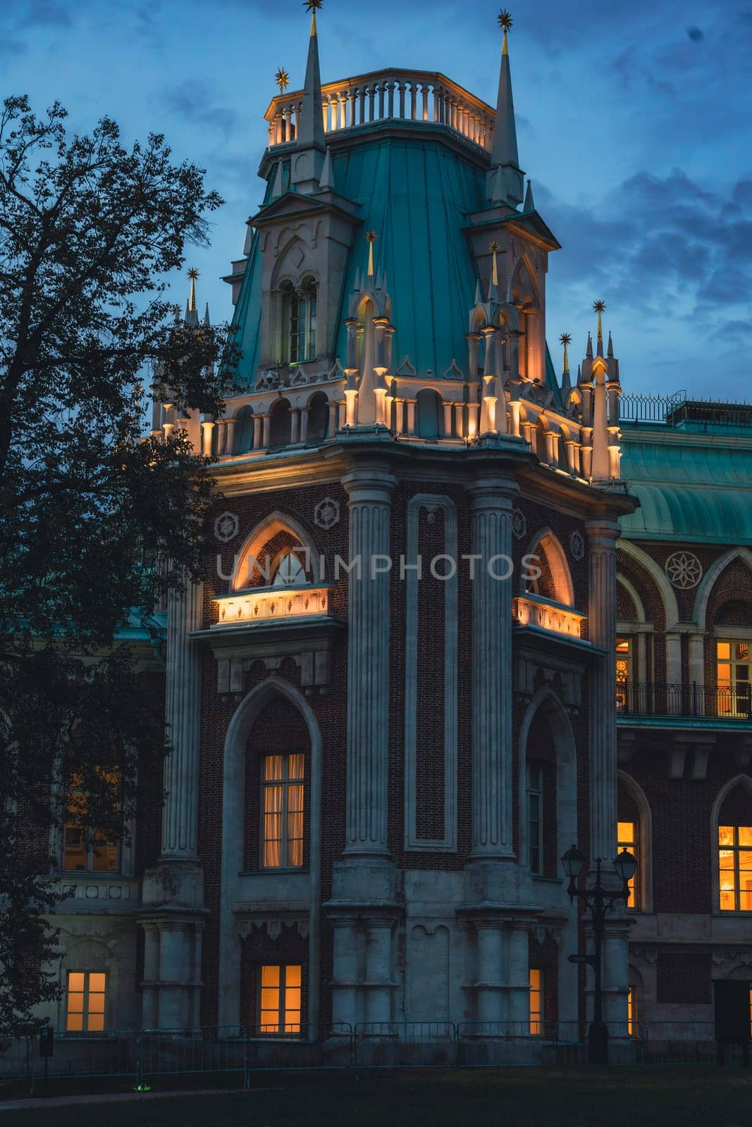 Close-up of a Gothic-style tower with arched windows and spires, warmly illuminated at dusk under a twilight sky.