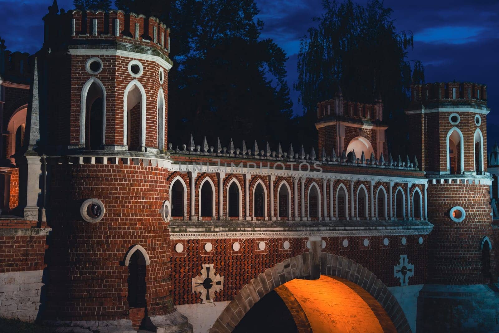 A Gothic-style brick bridge with illuminated arches and decorative towers, featuring intricate architectural details, captured at night.