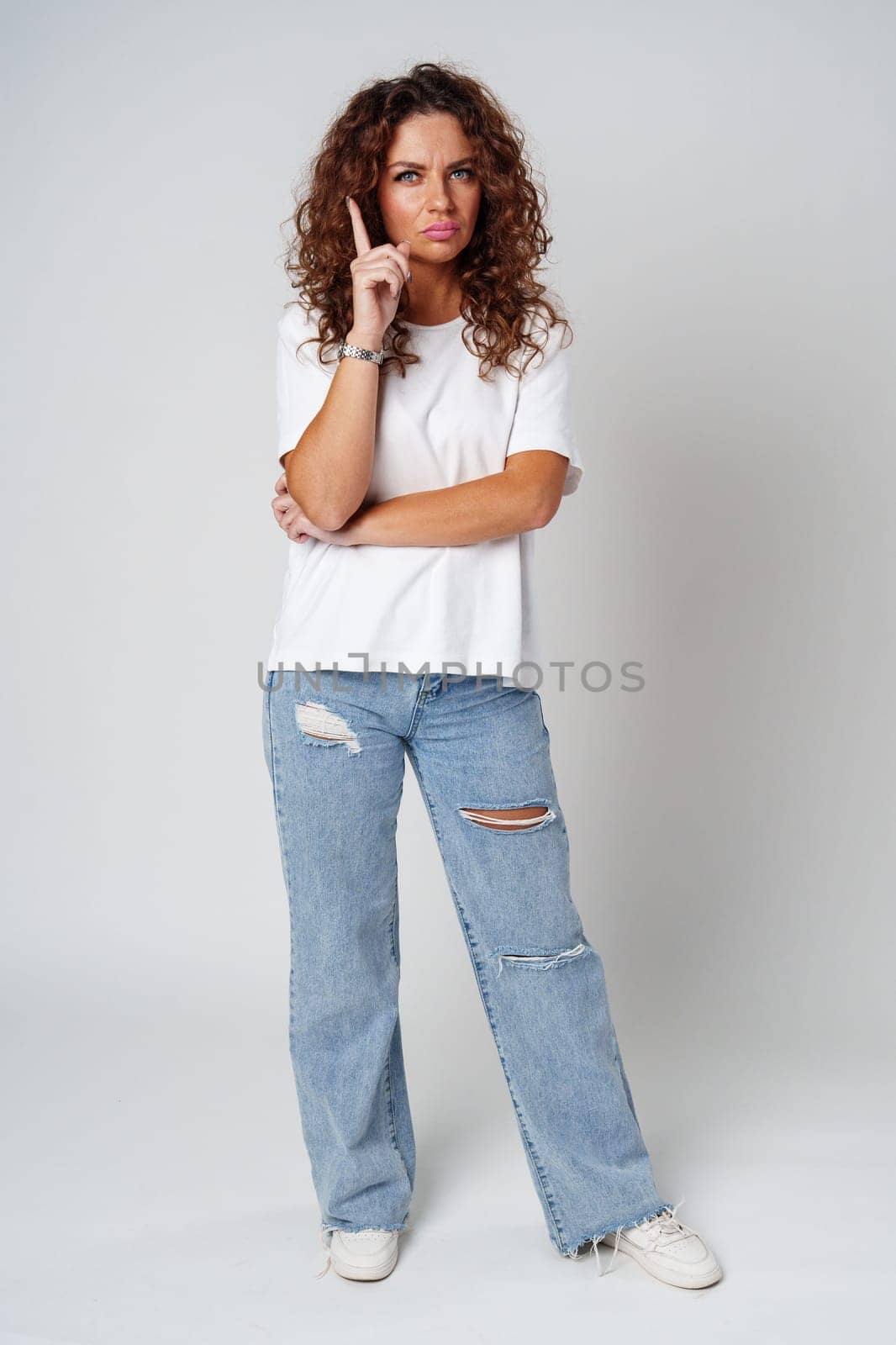 Woman with curly hair thoughtfully pondering in a neutral setting close up