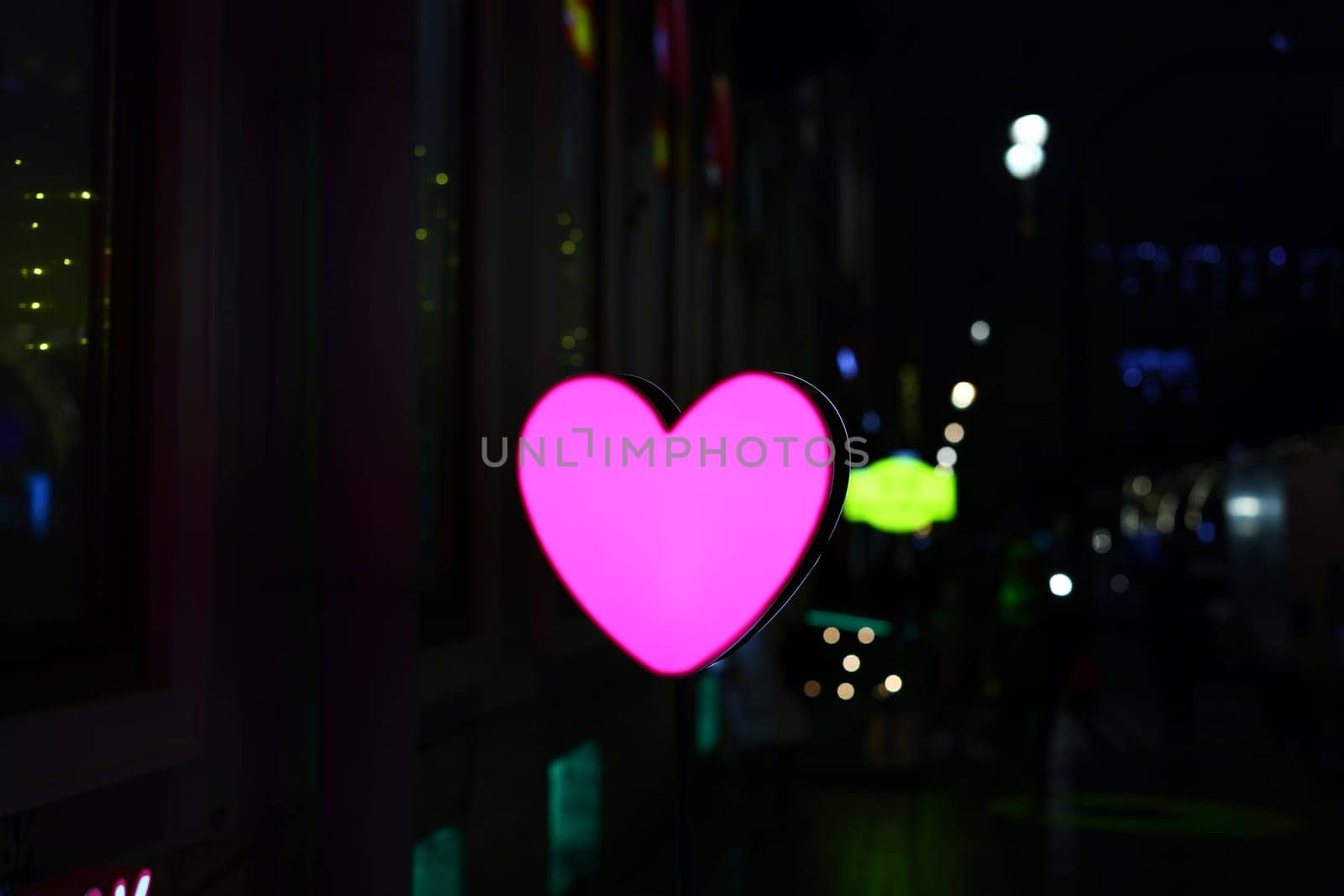 A glowing pink heartshaped decoration shines against a vibrant city backdrop at night, symbolizing love and nightlife