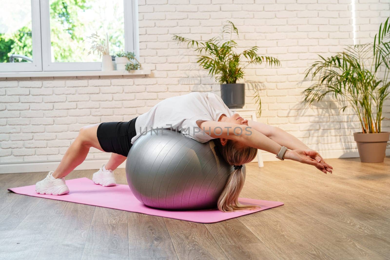 Young woman exercising on a stability ball in a bright room with plants close up