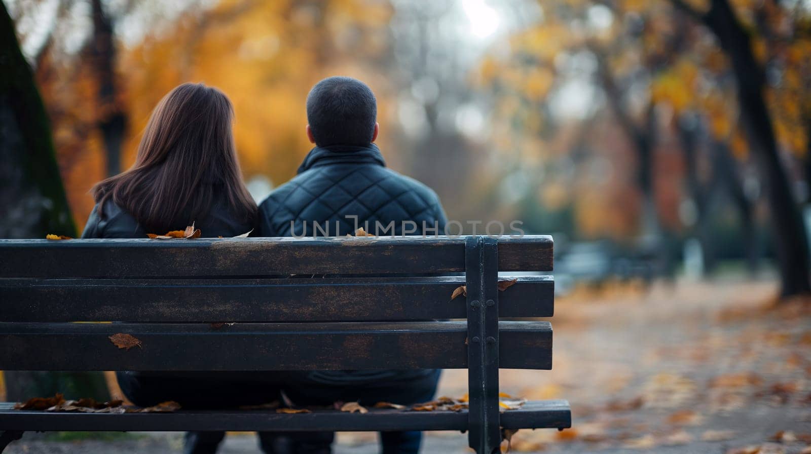 A couple sits closely together on a bench in a park, surrounded by colorful autumn foliage. The atmosphere is serene as they enjoy the beauty of the season - Generative AI