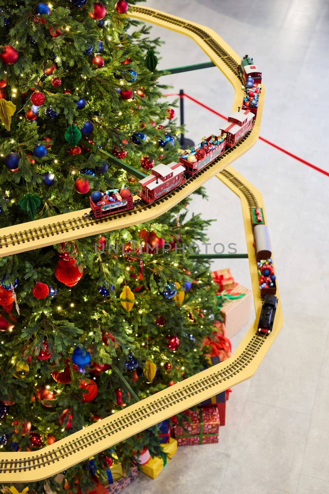 A brightly colored train set gracefully winds its way around a wonderfully decorated and vibrant Christmas tree