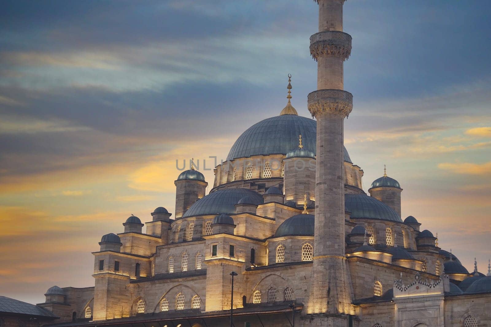 A beautifully lit mosque stands majestically under a vibrant sunset sky filled with colors