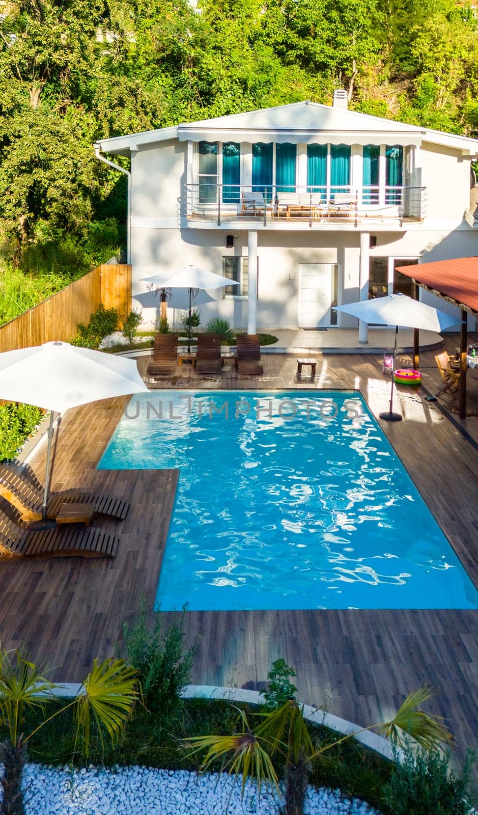 Modern backyard with swimming pool, wooden deck, and lush greenery surrounding a stylish two-story house