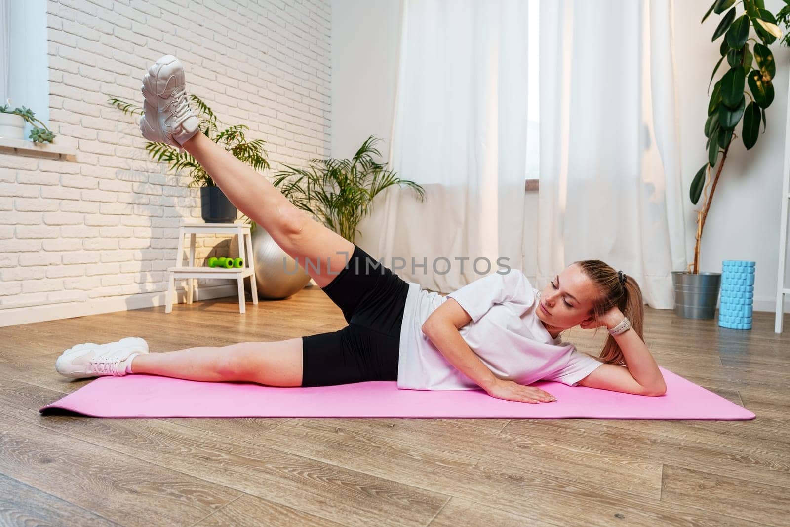 Woman doing floor exercises on a pink mat in a bright, plant-filled room
