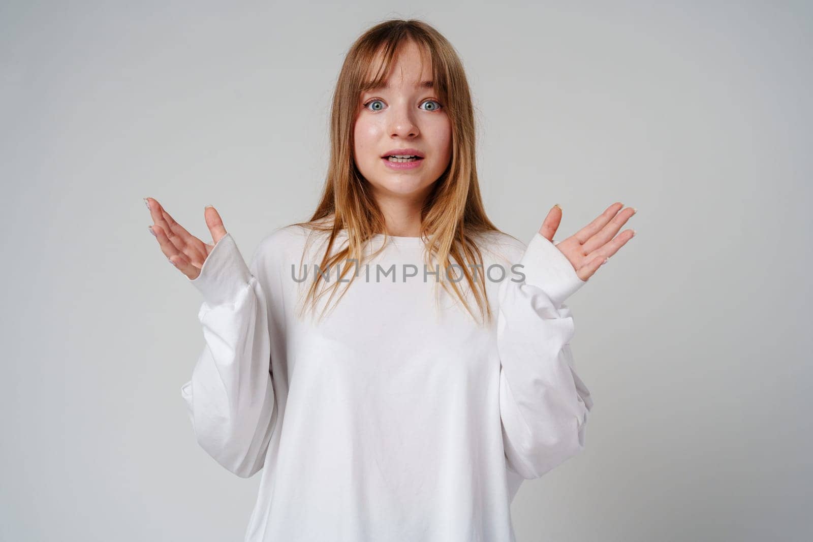 A surprised child wearing a white long-sleeve shirt and blue jeans expresses confusion in a studio setting close up