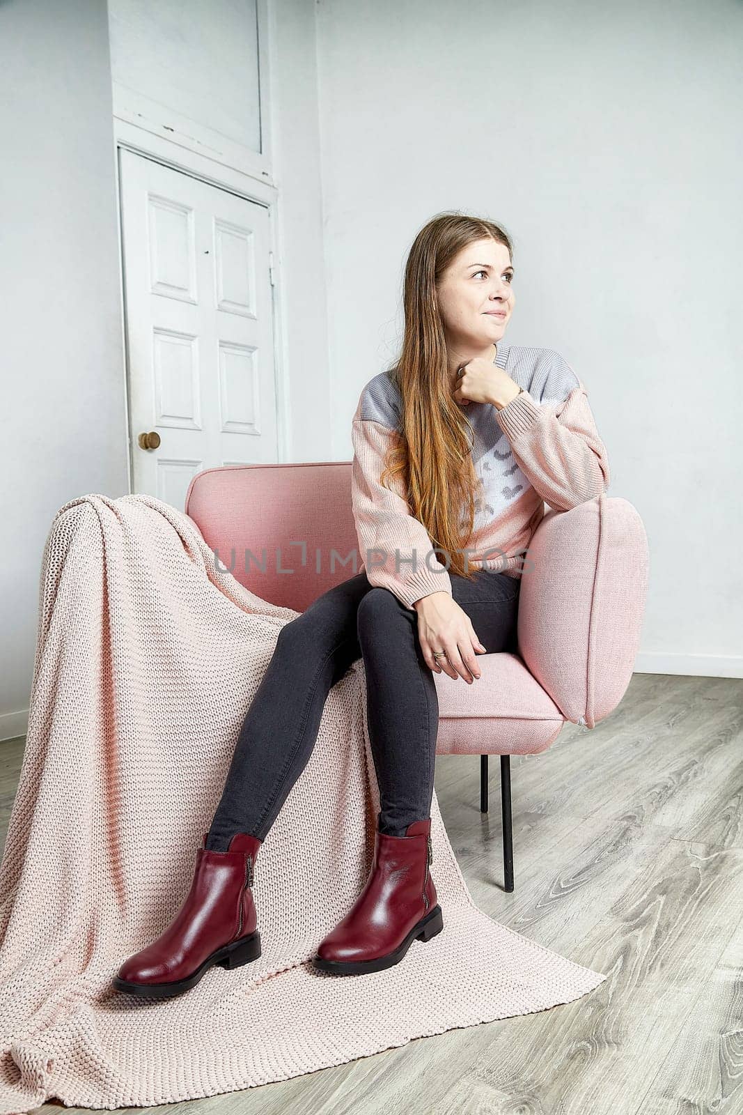 A model poses thoughtfully on a pink couch, showcasing trendy shoes, in a minimalist room with natural light.