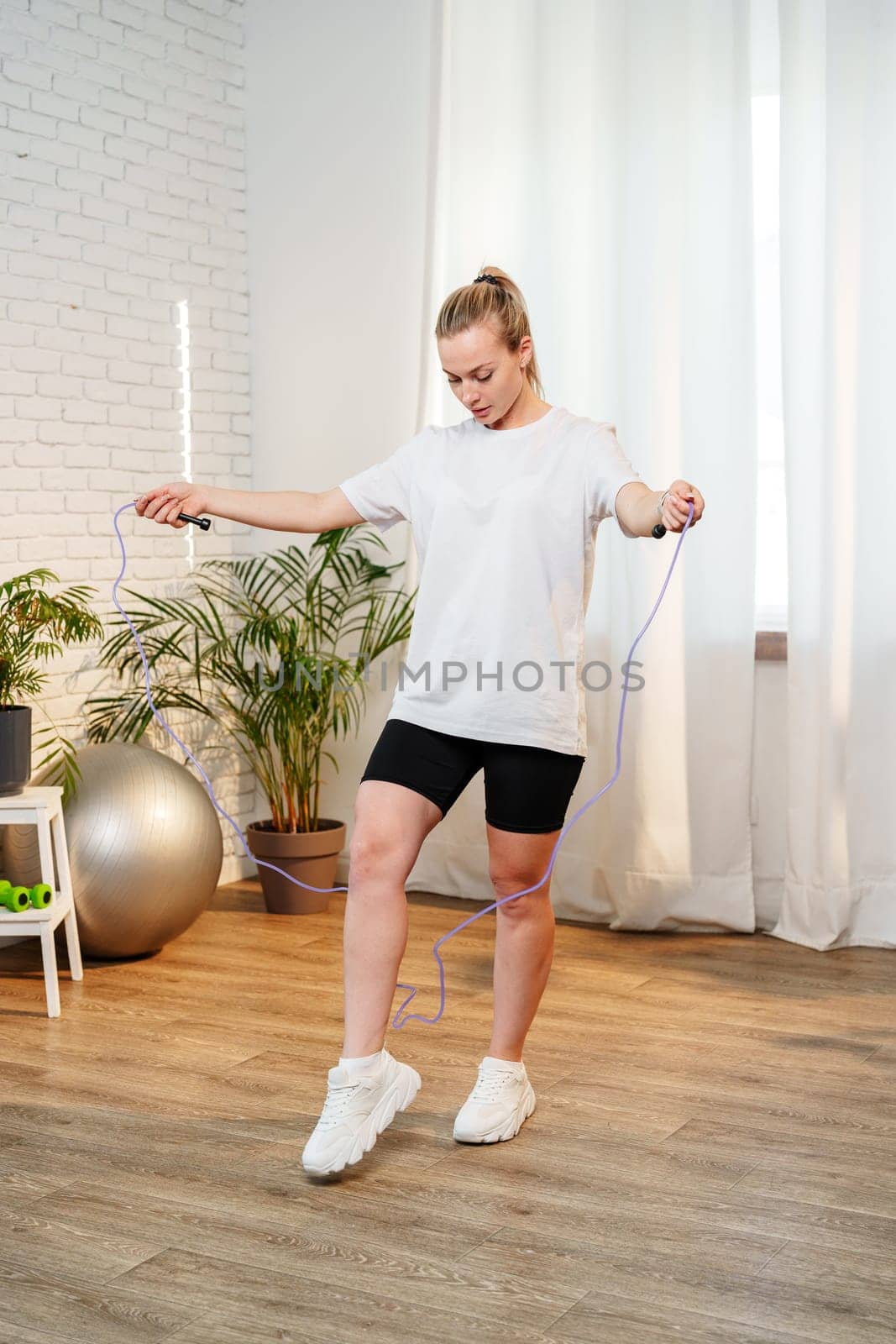 A woman skipping rope in a bright living room filled with plants close up