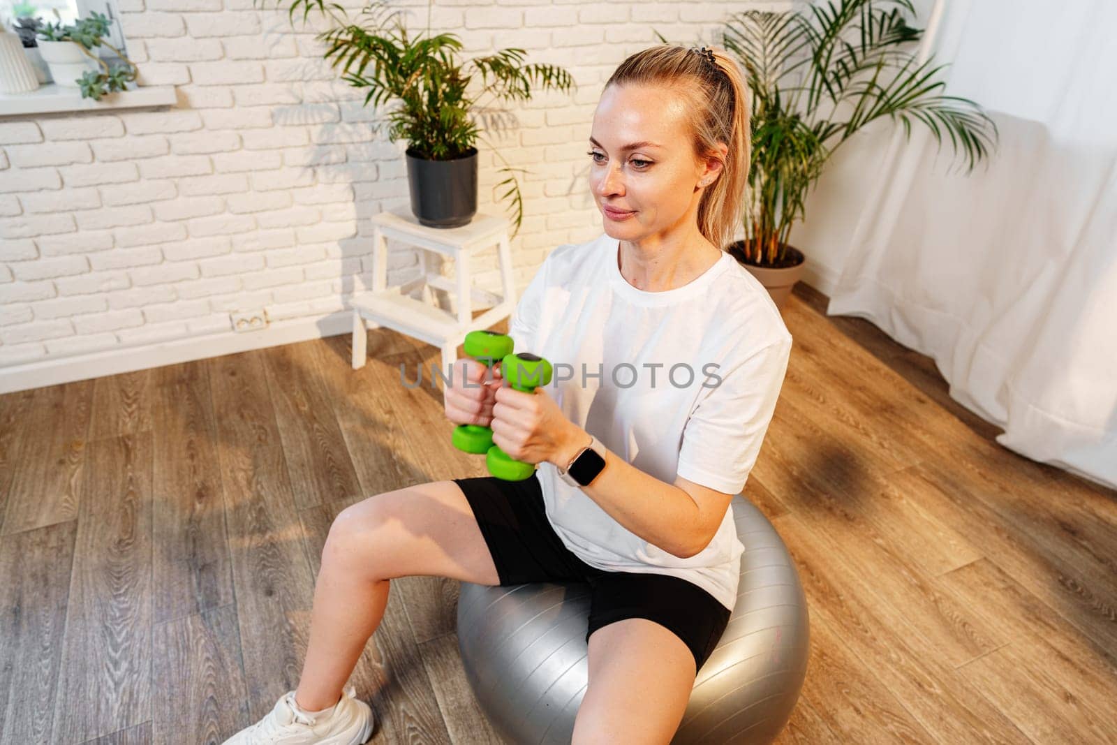 Woman exercising with dumbbells on a stability ball in a bright indoor space