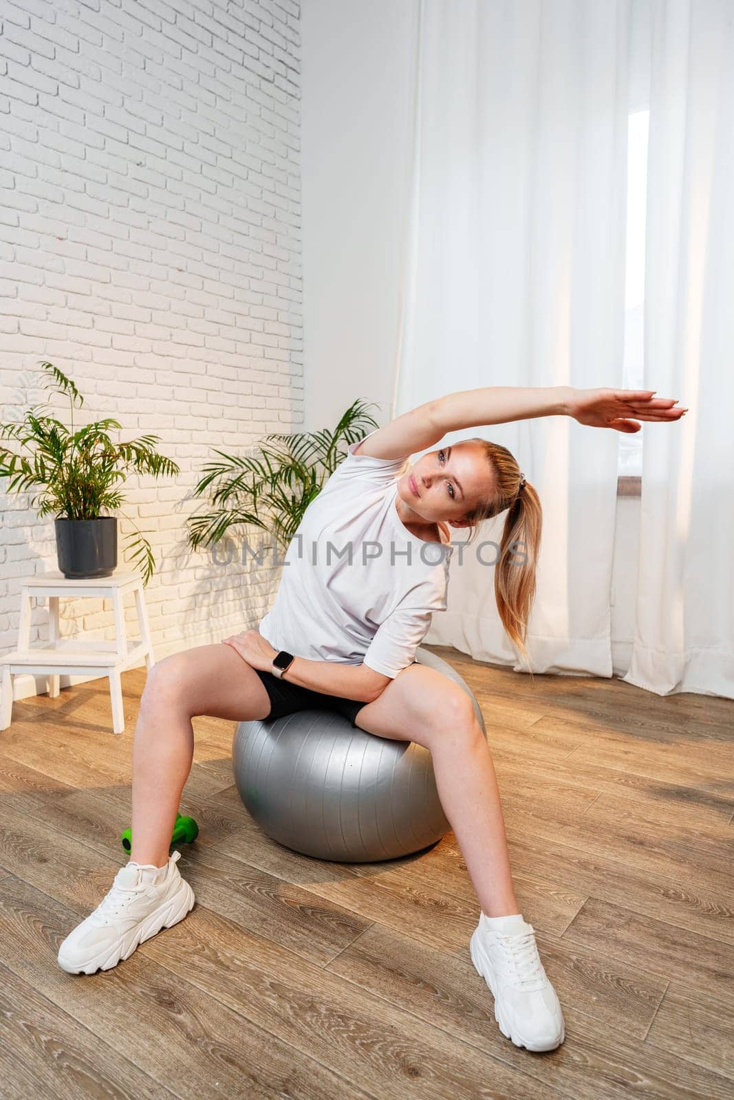 A woman stretching sideways in a bright, minimalist room with indoor plants