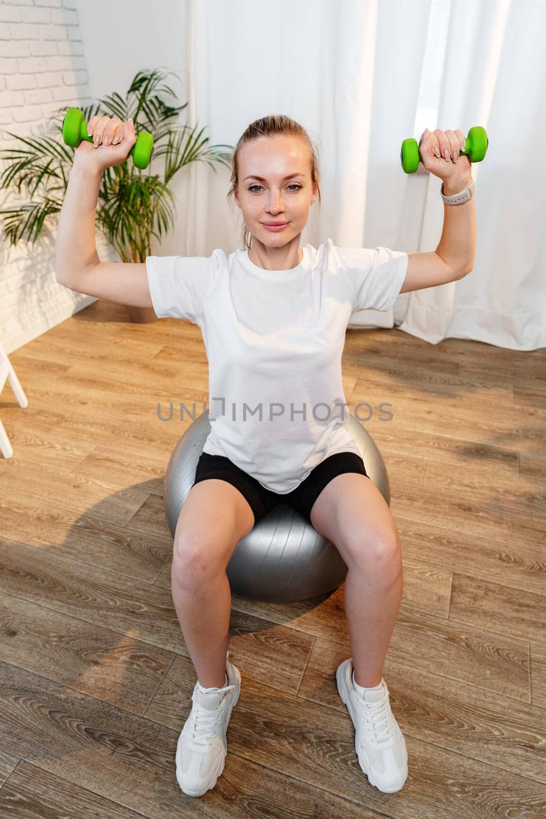 Woman exercising with dumbbells on a stability ball in a bright indoor space
