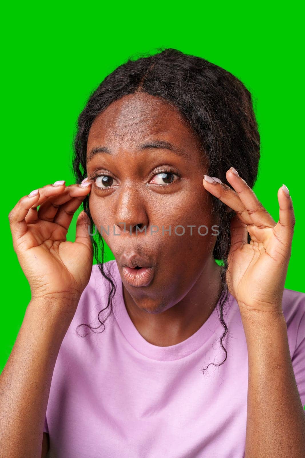 Surprised woman expressing shock while posing with hands on her face against a bright green backdrop close up