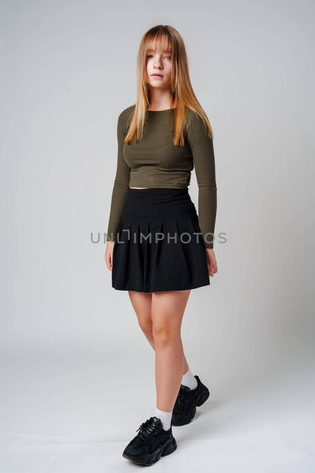 A young woman with straight hair wearing a green top poses against a neutral background in a calm setting