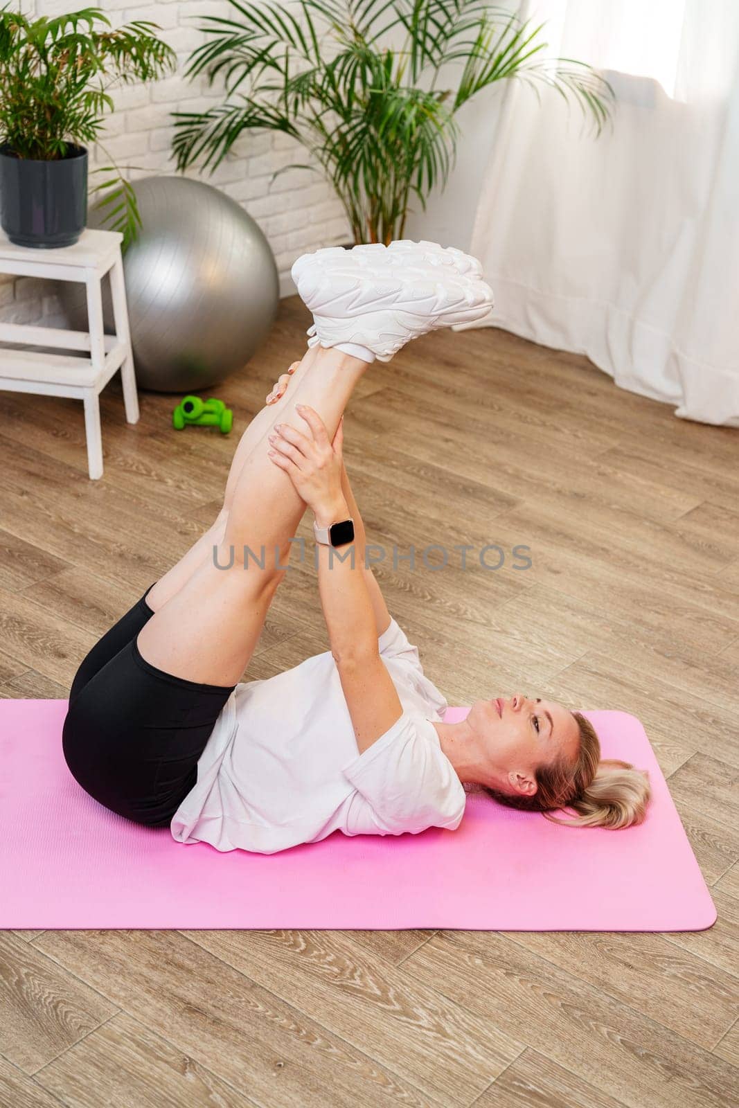Woman doing floor exercises on a pink mat in a bright, plant-filled room