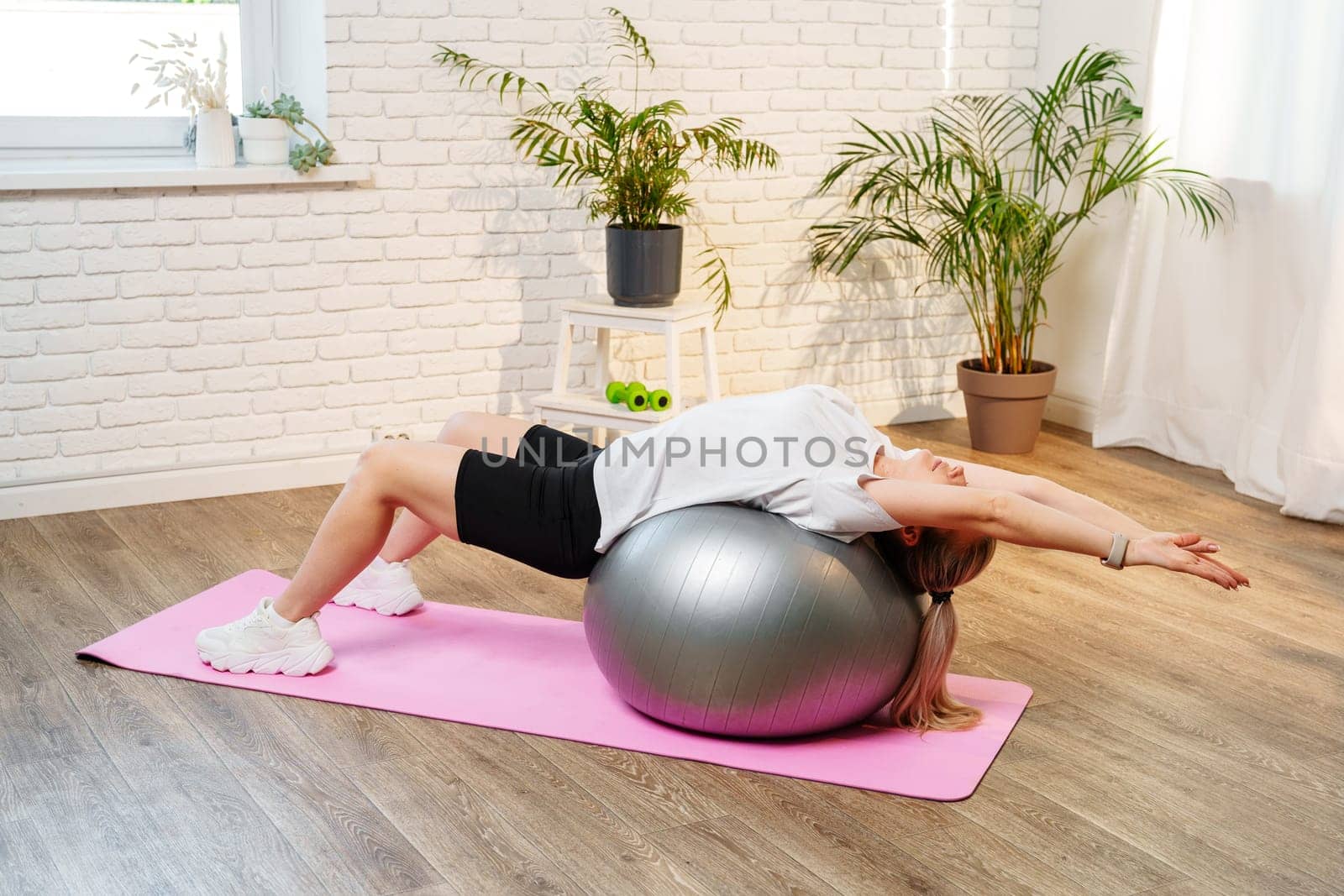 Young woman exercising on a stability ball in a bright room with plants close up