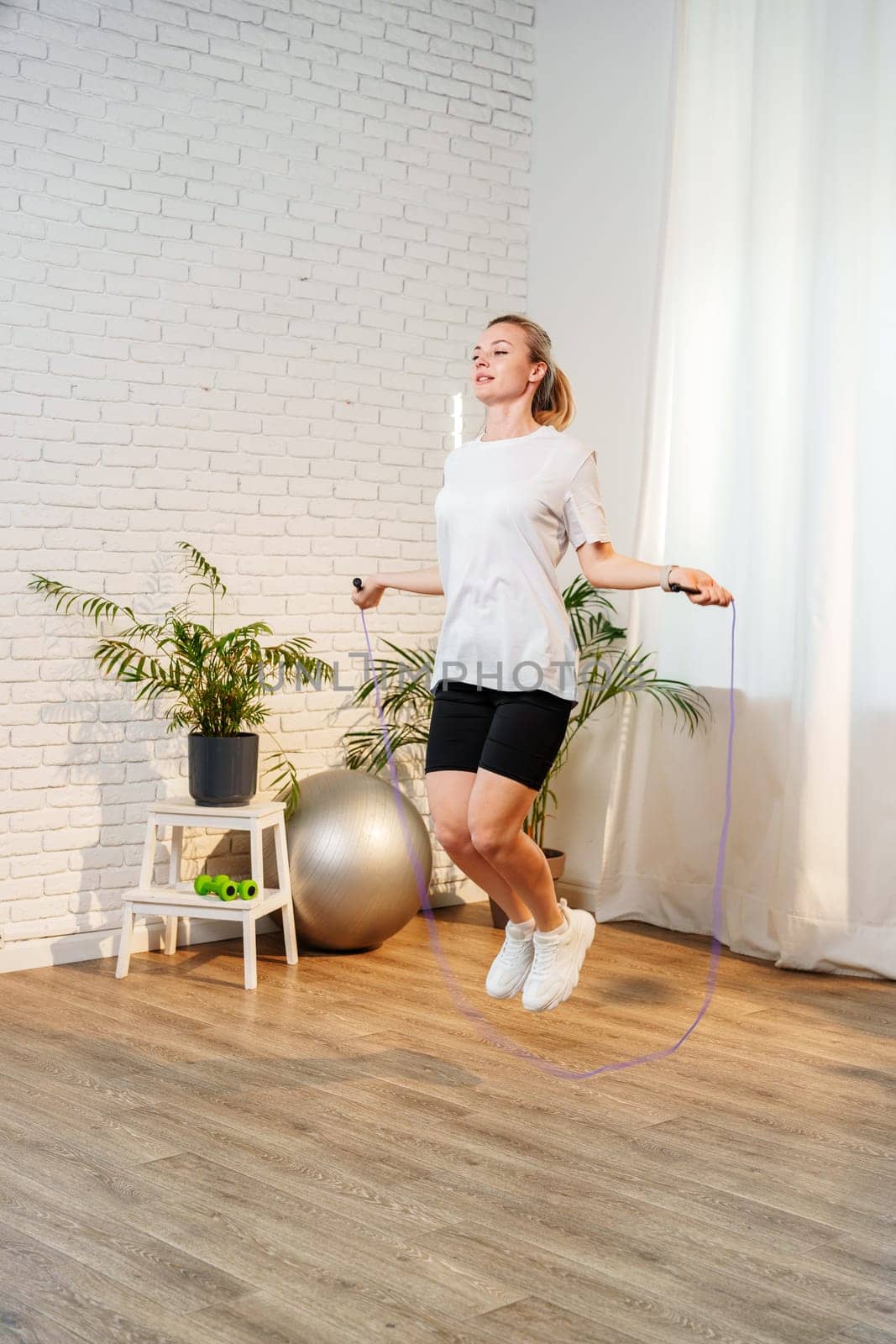 A woman skipping rope in a bright living room filled with plants close up