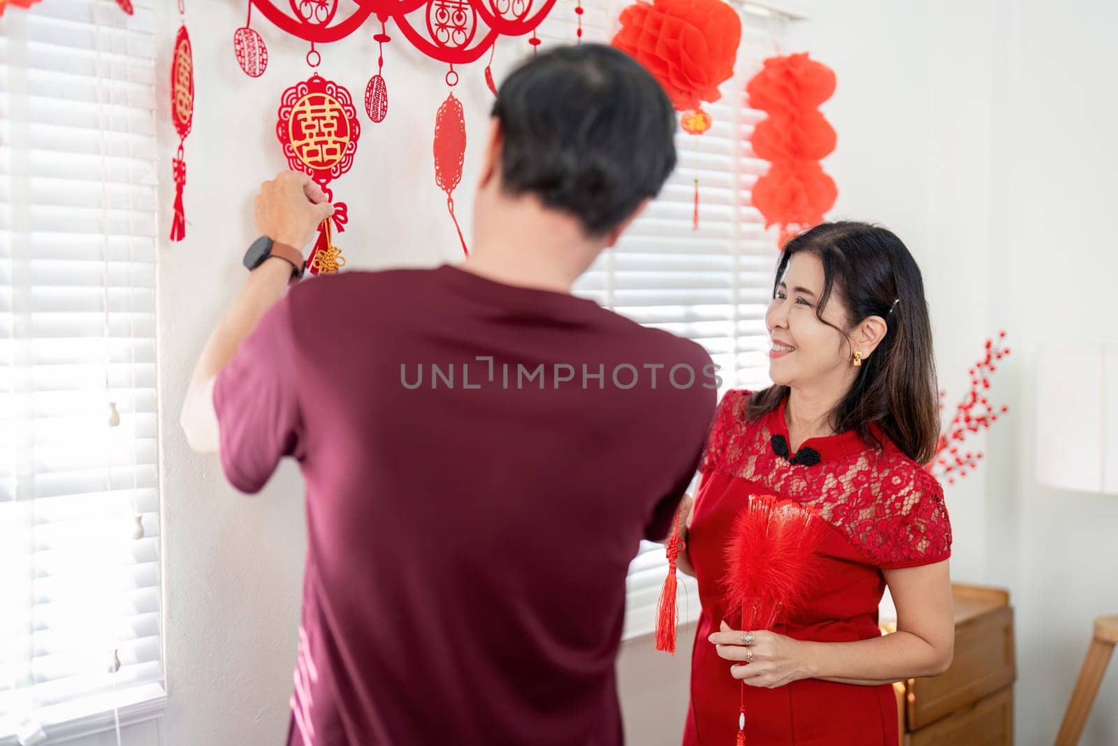An elderly couple joyfully decorates their home for Chinese New Year embracing traditions and sharing love in a cozy setting.