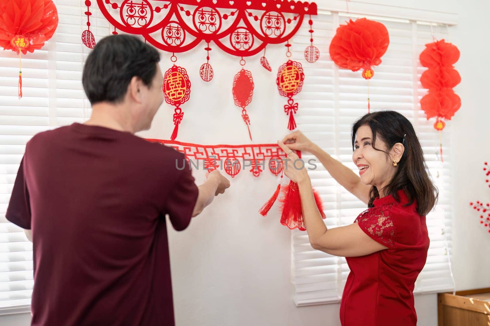 An elderly couple joyfully decorates their home for Chinese New Year celebrating traditions and family togetherness.