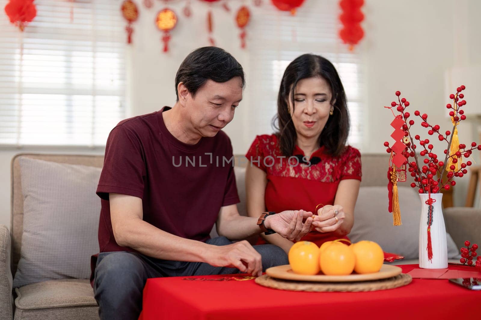 An elderly couple engages in joyful Chinese New Year traditions surrounded by festive decor and oranges symbolizing prosperity.
