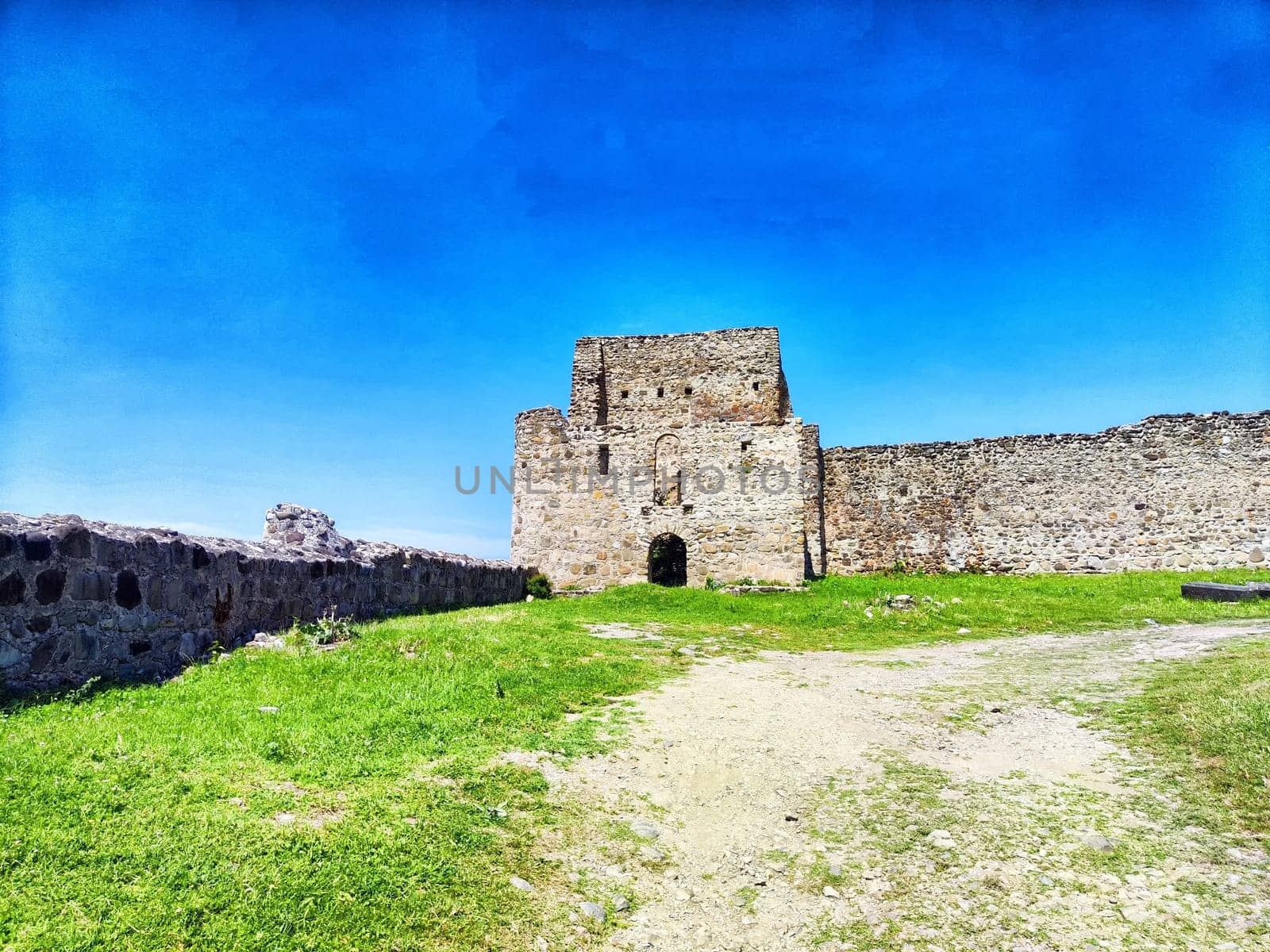 A majestic stone fortress overlooks a vibrant green field while nestled under a bright blue sky, showcasing its historical significance.