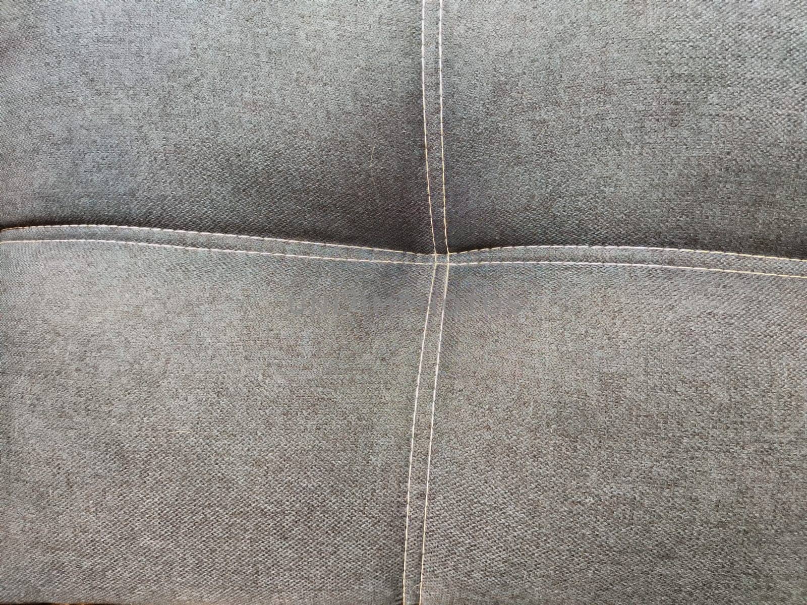 A smooth gray fabric features a textured pattern with visible stitching, ideal for showcasing interior design projects or upholstery work.