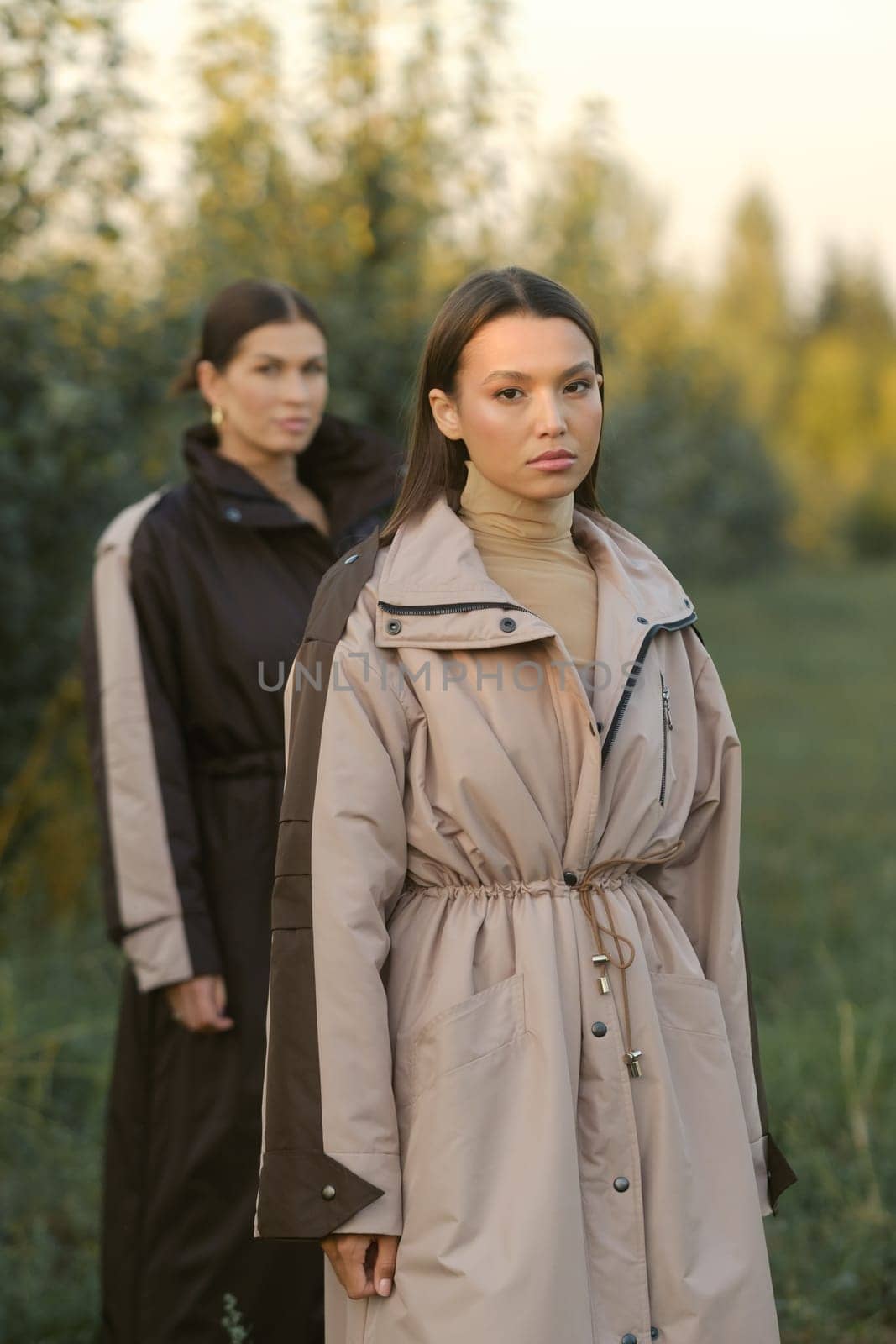 Two stylish girls in raincoats in an apple orchard. Fashion show in an orchard.