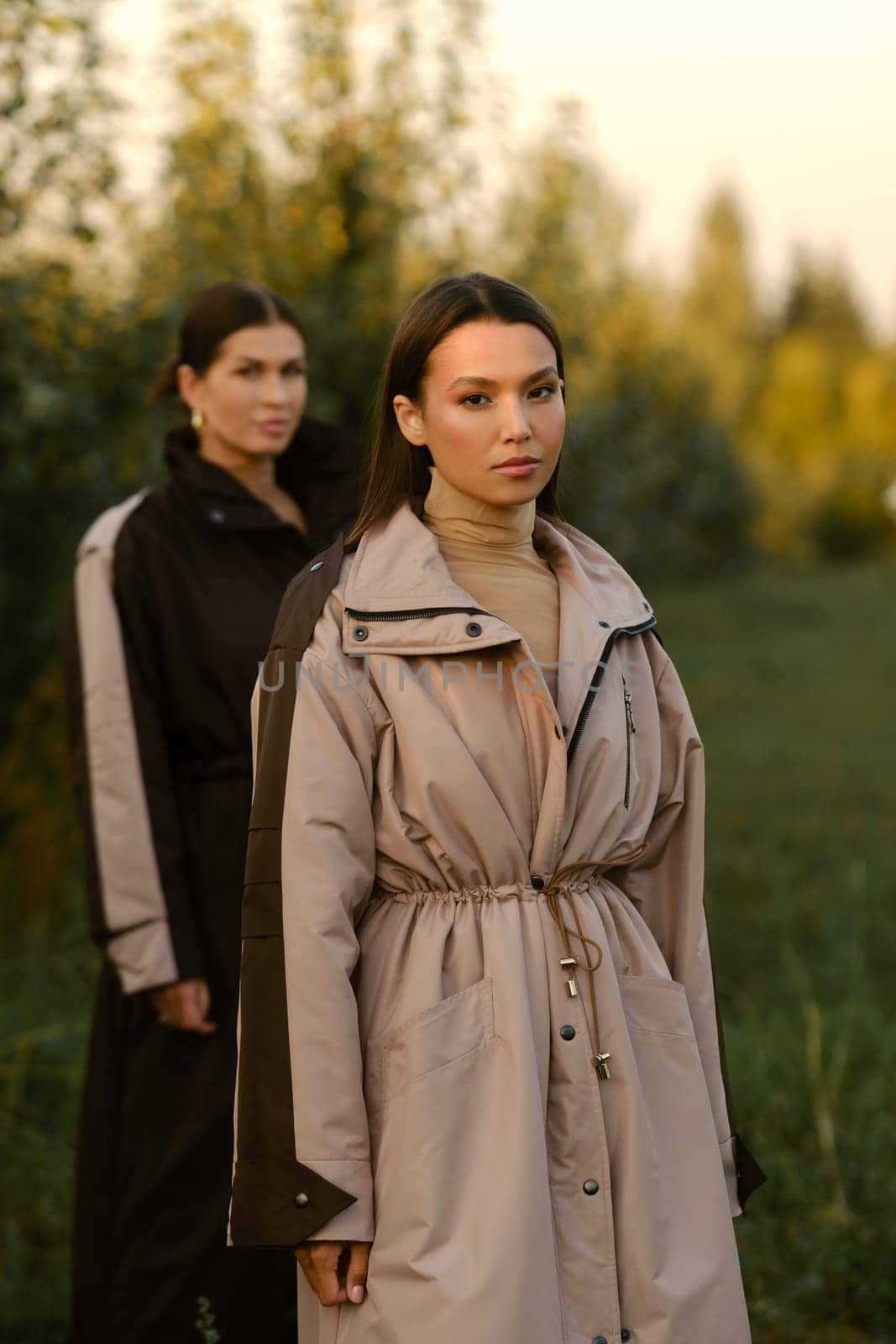 Two stylish girls in raincoats in an apple orchard. Fashion show in an orchard.