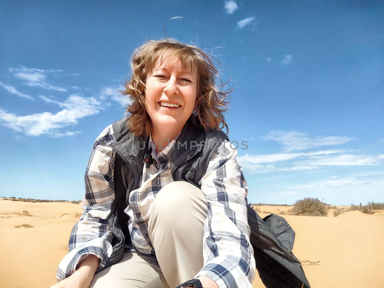 A middle aged woman enjoys the warm sunshine while seated on the sand, surrounded by the vast desert landscape.