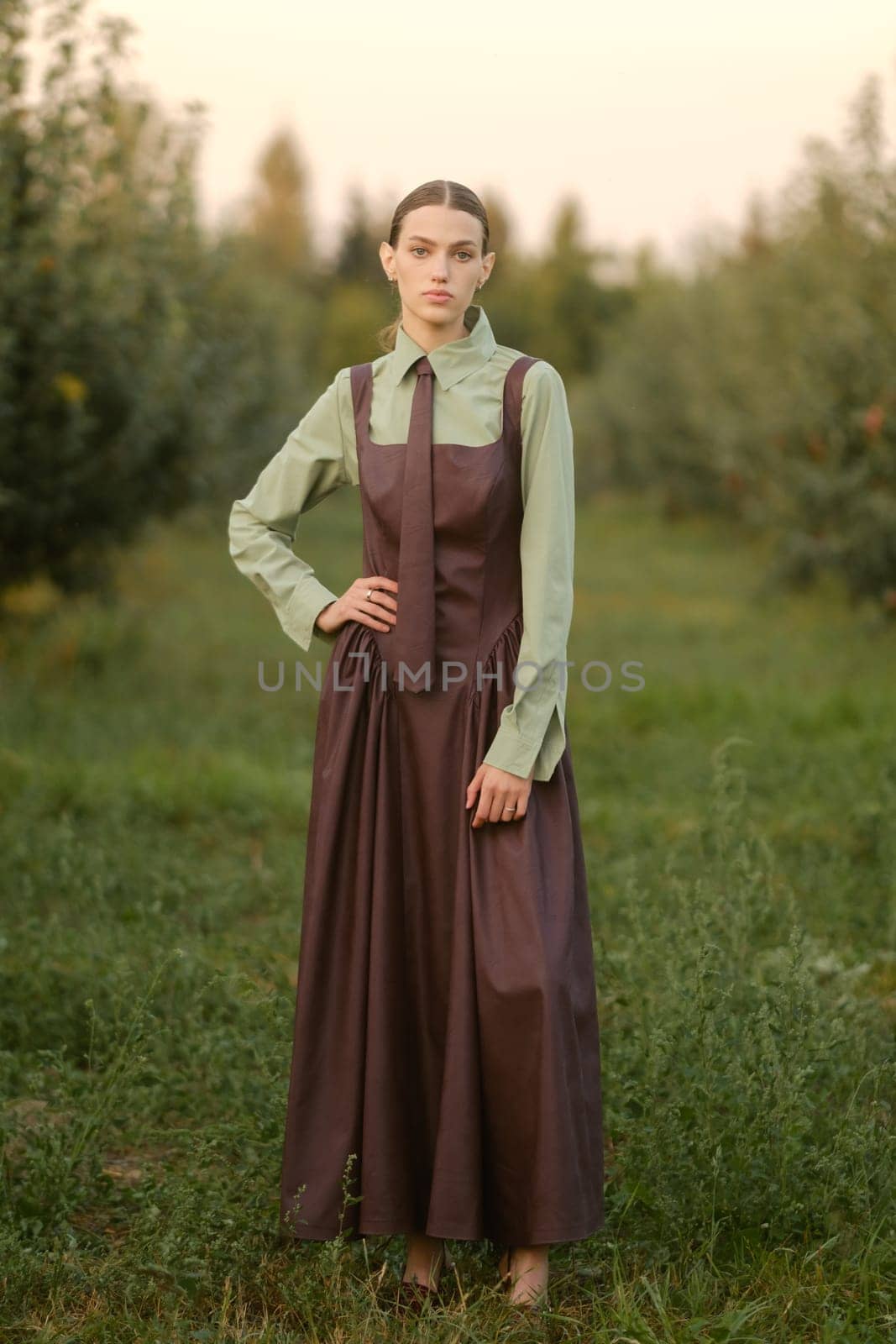 A stylish girl in a dress with a tie in a summer garden. A fashion show in nature.