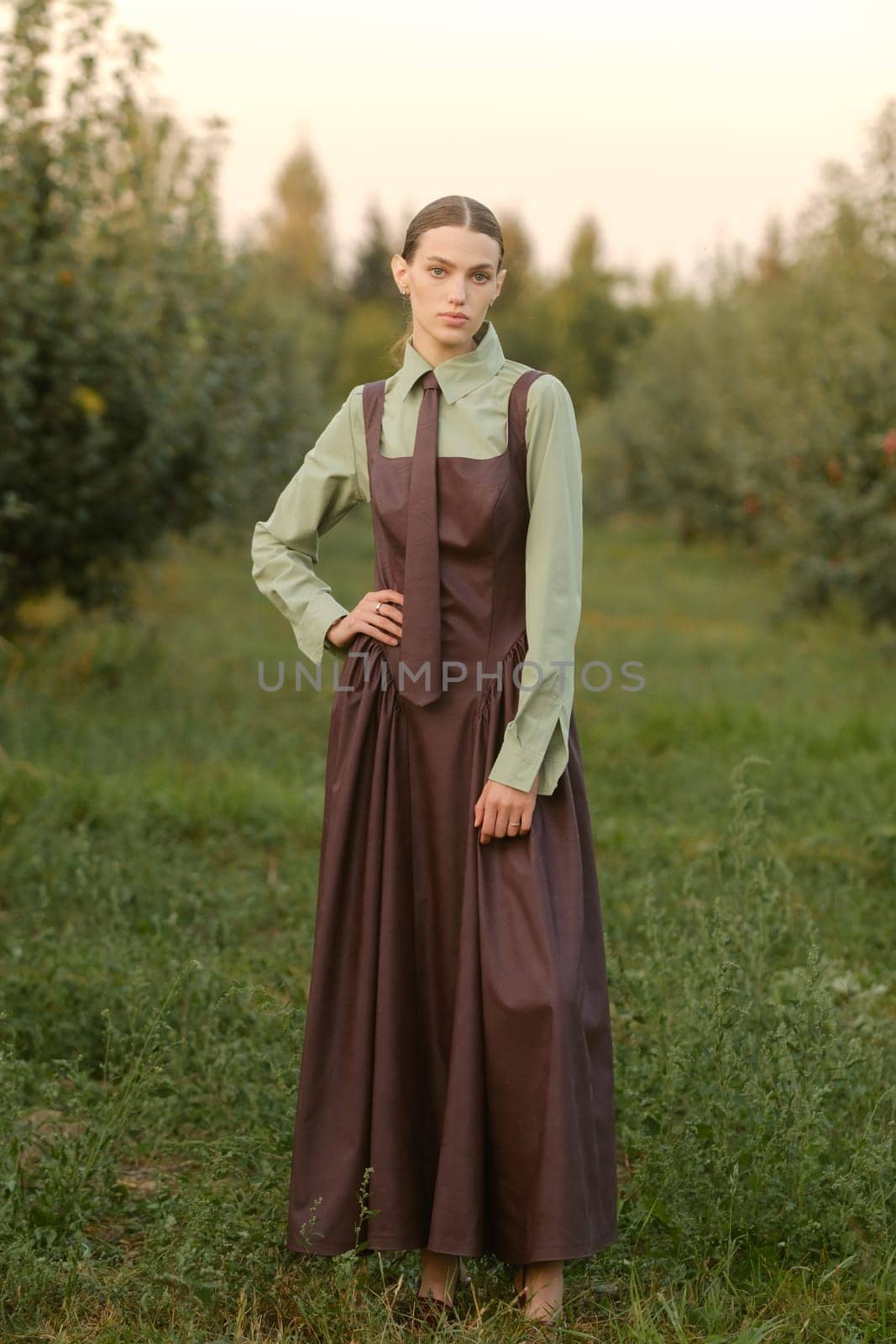 A stylish girl in a dress with a tie in a summer garden. A fashion show in nature.