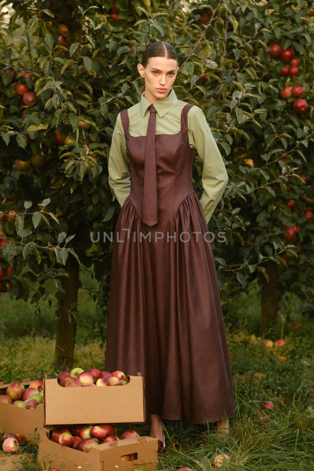 Portrait of a beautiful girl, stylishly dressed, with apples in the garden. A girl stands near the collected red apples in the garden.