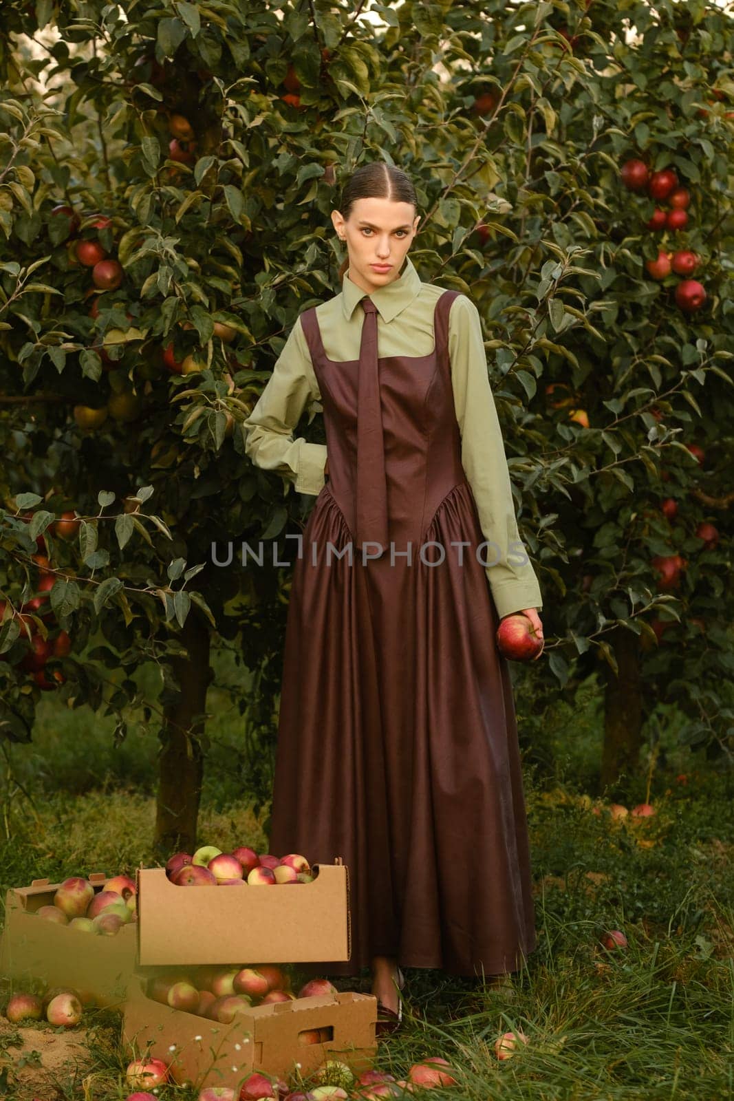 Portrait of a beautiful girl, stylishly dressed, with apples in the garden. A girl stands near the collected red apples in the garden.