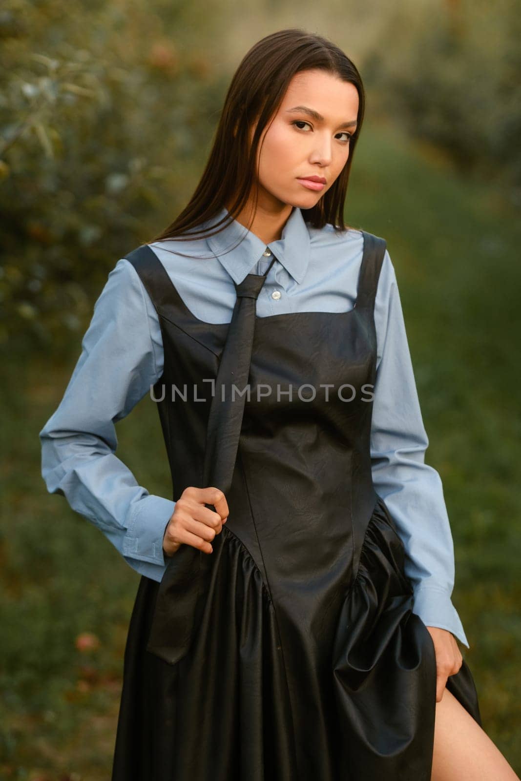 A stylish girl in a dress with a tie in a summer garden. A fashion show in nature.