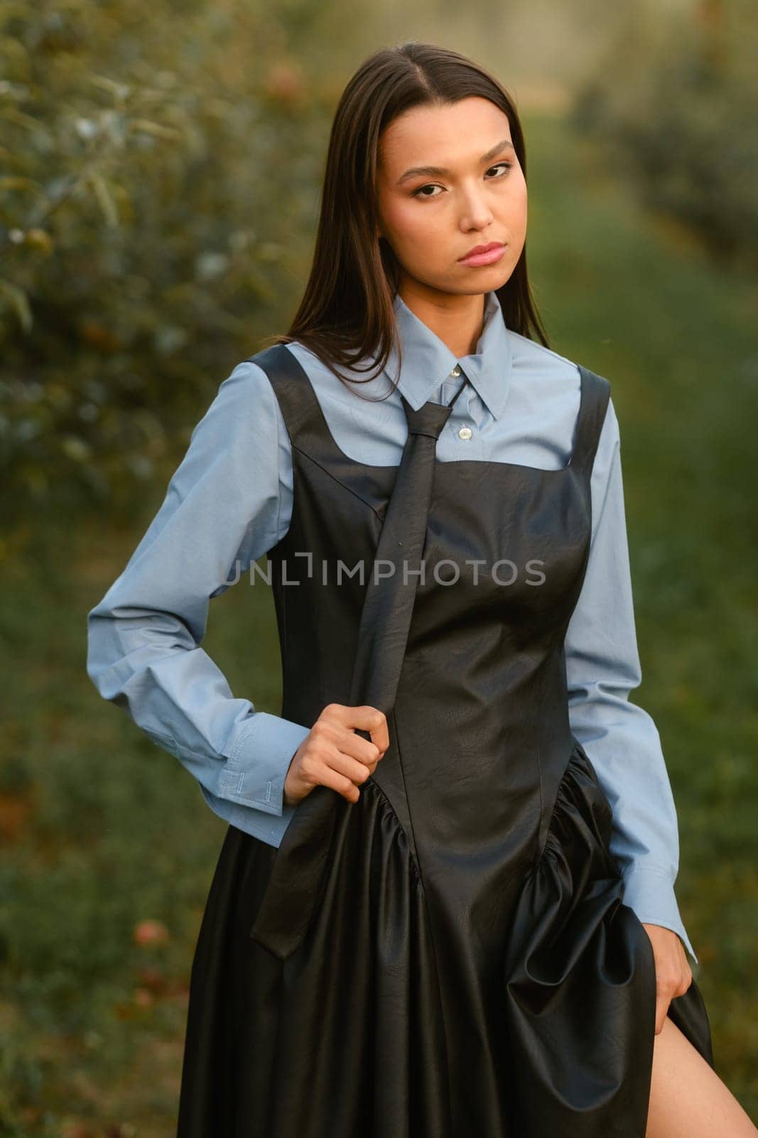 A stylish girl in a dress with a tie in a summer garden. A fashion show in nature.