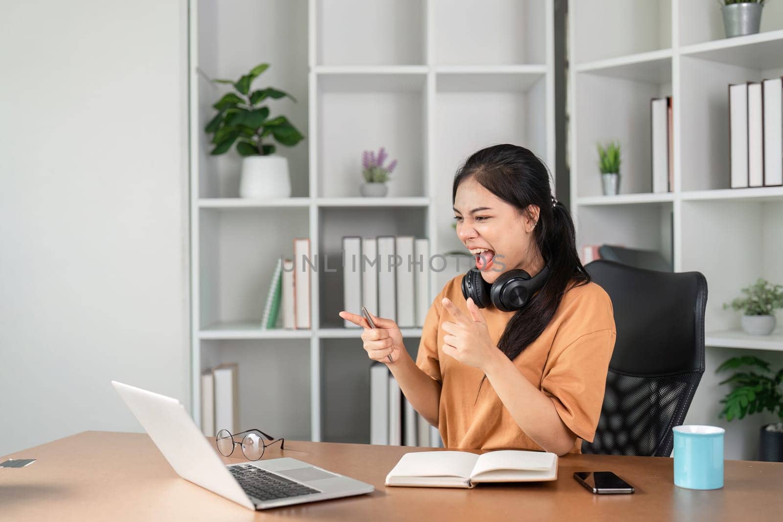 A young female employee celebrates success at her desk, expressing joy and excitement in a modern office setting.