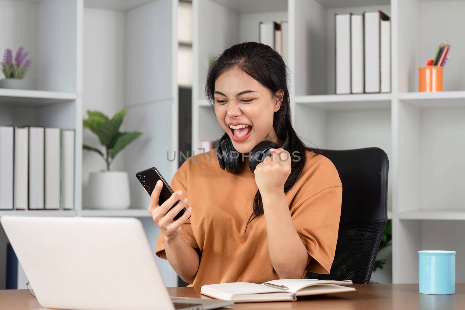 A young female employee joyfully celebrates a professional success in a modern office environment, showcasing happiness and achievement.