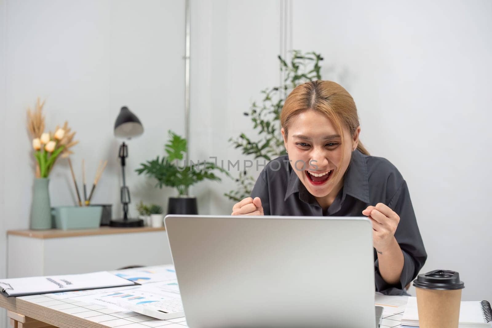 A joyful businesswoman expressing delight at her professional success while working in a contemporary office setting.
