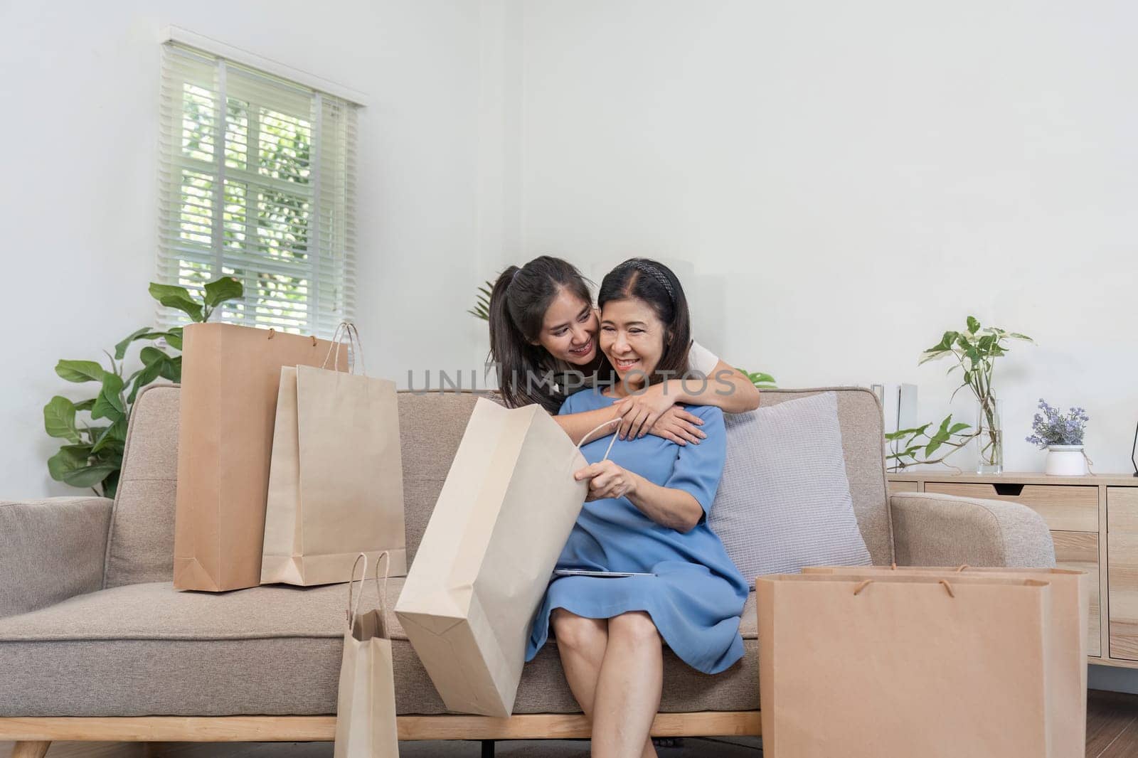 A happy mother and child share a joyful moment with paper shopping bags, sitting on a comfortable sofa in a modern living room.