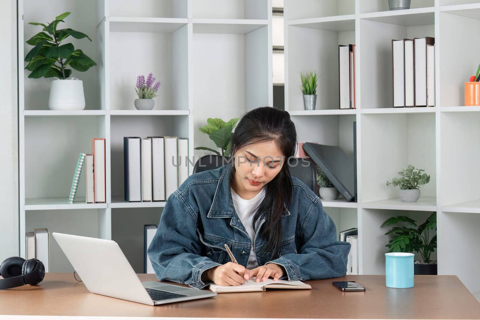 A young woman diligently doing homework at her desk with a laptop and books, creating a productive study environment.