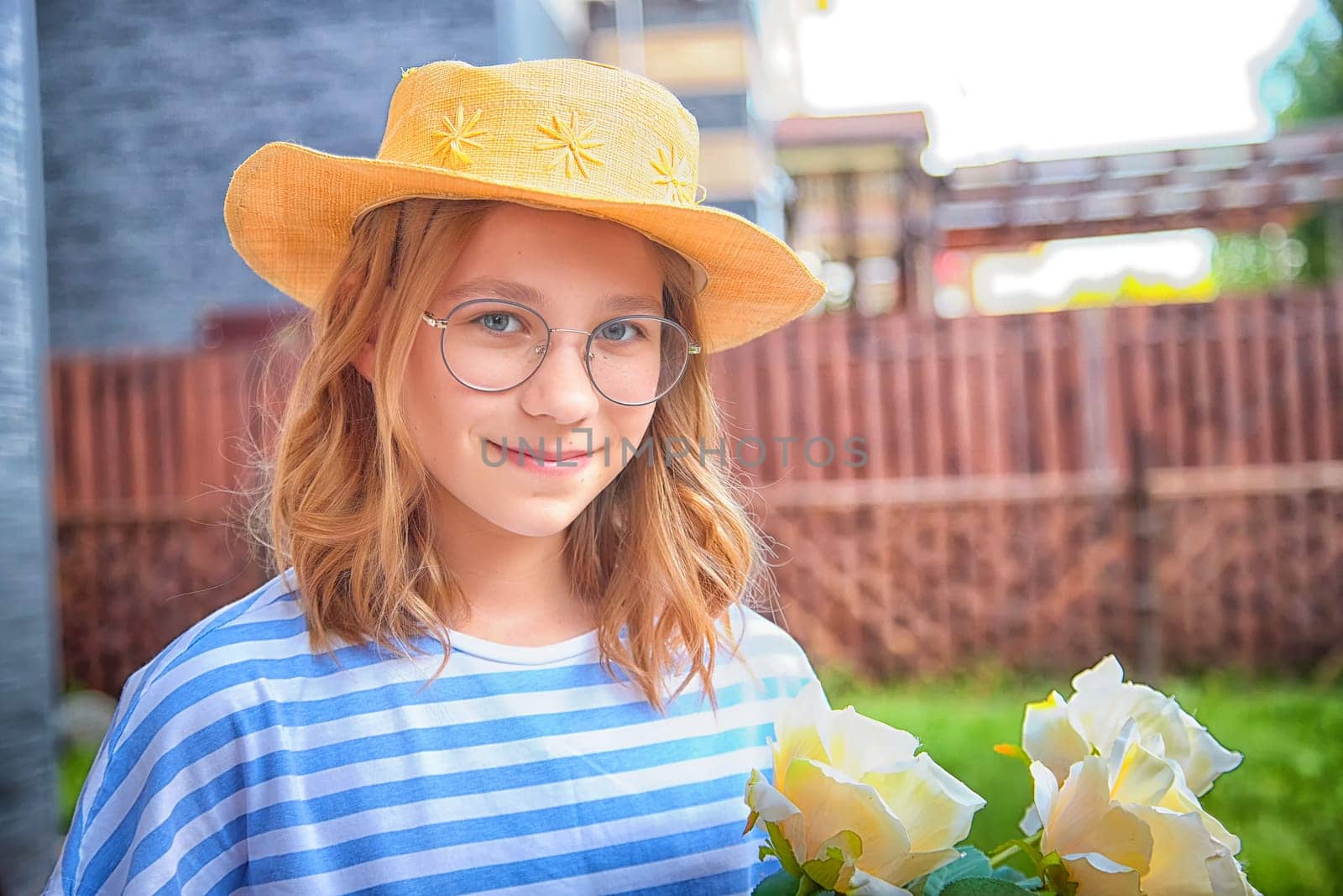 A girl wearing a striped shirt and glasses smiles while holding a bouquet of white roses in a garden.