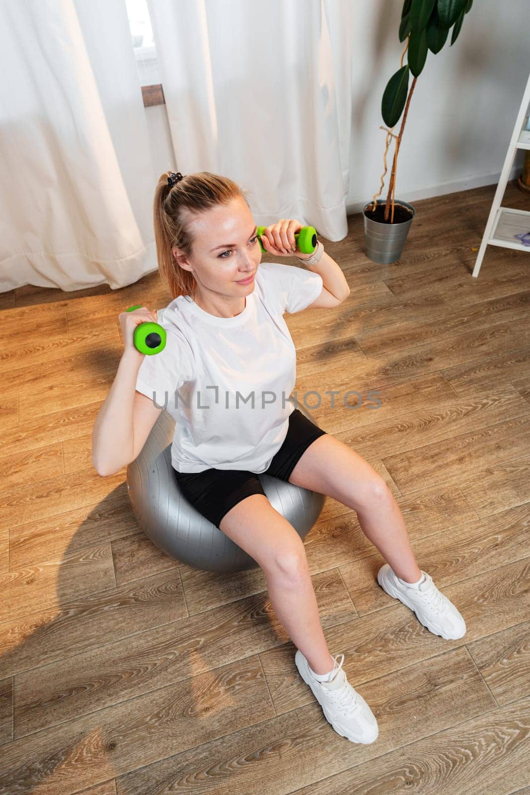 Woman exercising with dumbbells on a stability ball in a bright indoor space