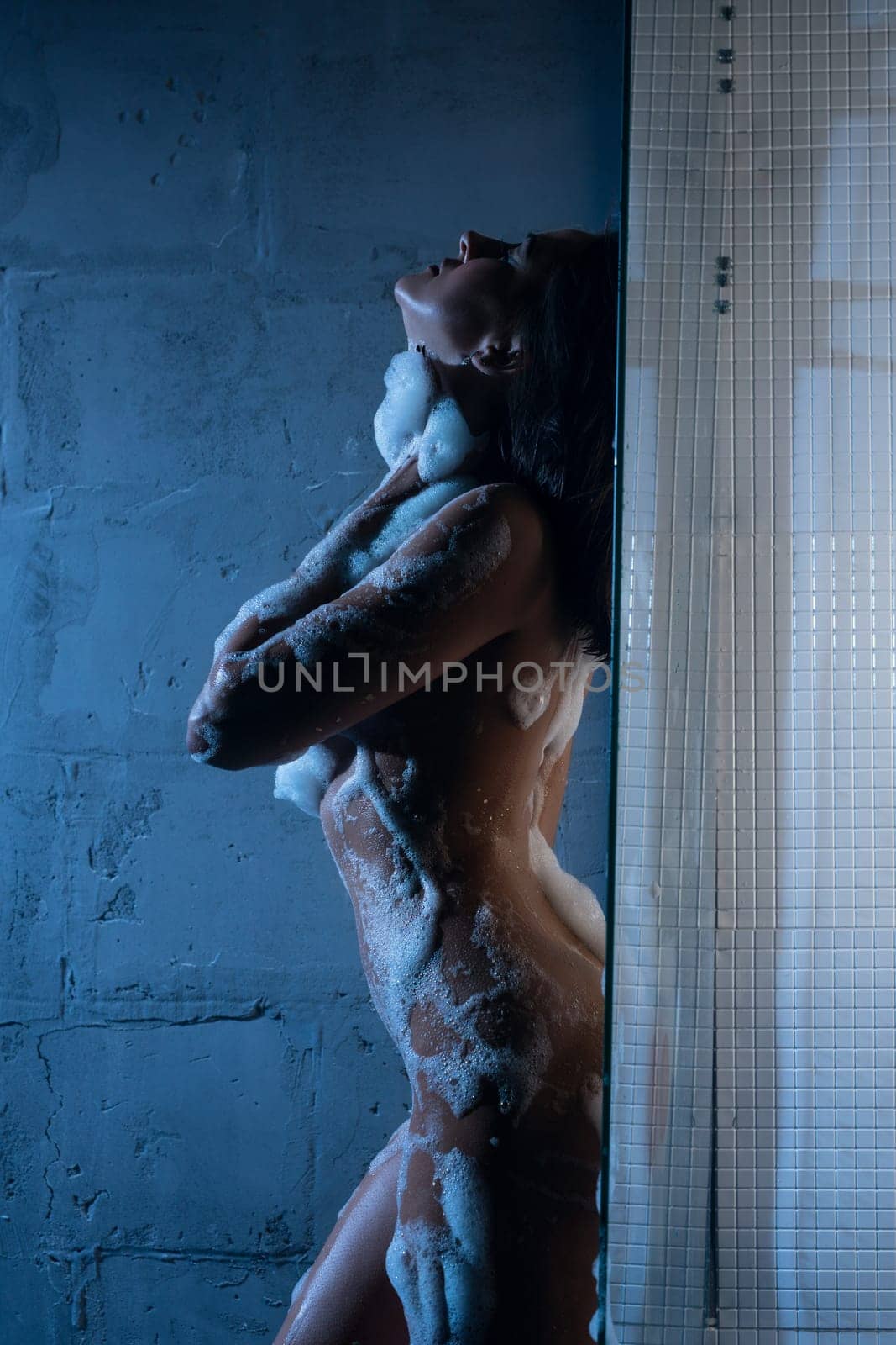 Nude girl in white foam profile view against white wall