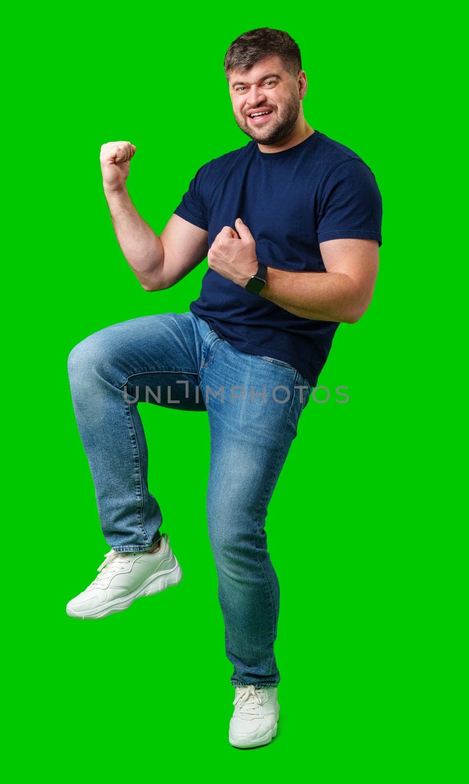 A strong man with fists raised, smiling confidently, on a bright green background in studio