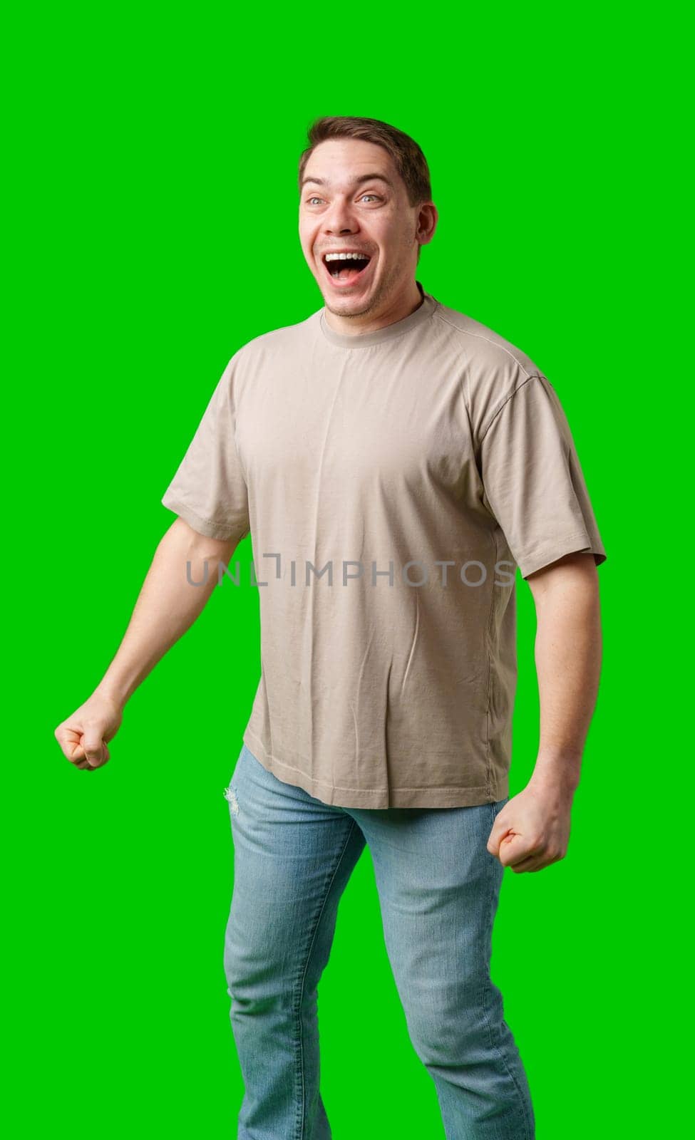 Young man in casual clothing stands with open arms against a vibrant green background in studio